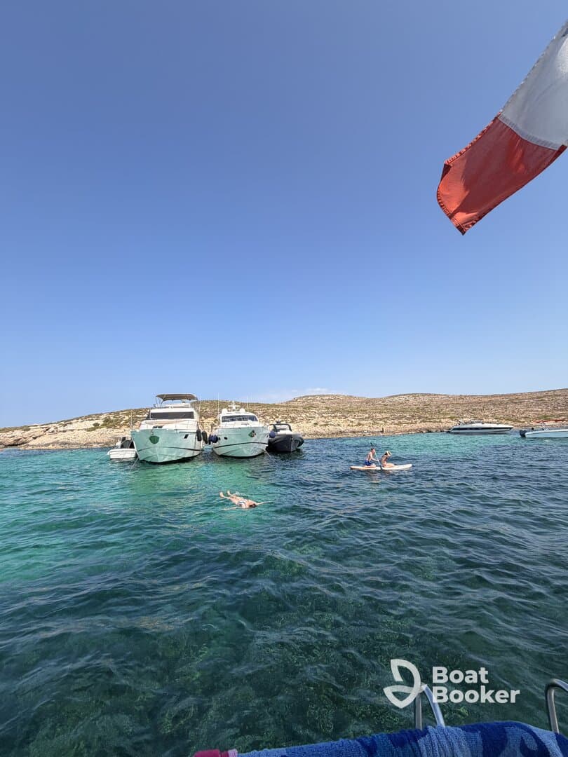Guests enjoy a sunny day at a picturesque sandbar, with some swimming and others paddleboarding among anchored boats in crystal-clear waters.