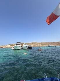 Guests enjoy a sunny day at a picturesque sandbar, with some swimming and others paddleboarding among anchored boats in crystal-clear waters.