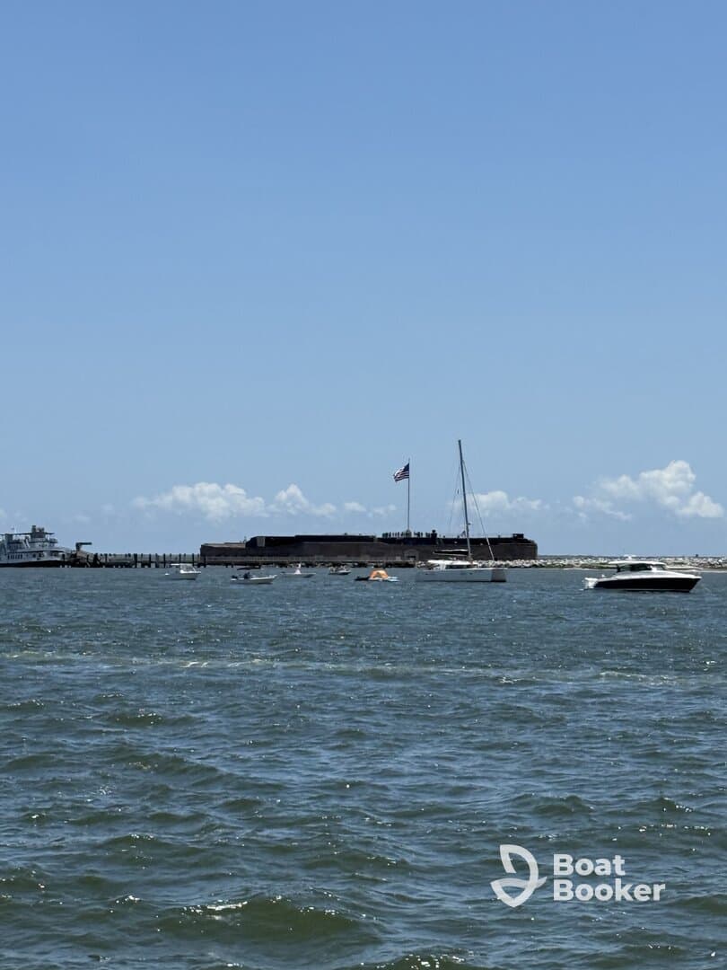 A scenic view of a harbor with various boats sailing near a historic fort, showcasing the beauty of a day on the water.