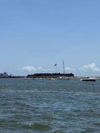 A scenic view of a harbor with various boats sailing near a historic fort, showcasing the beauty of a day on the water.