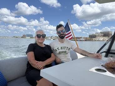 A couple enjoys a relaxing moment aboard a boat, with scenic views of the waterfront and a clear blue sky in the background.