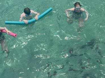 Two children enjoy a fun day in the clear waters, playing with pool noodles — a perfect family-friendly activity for summer adventures.