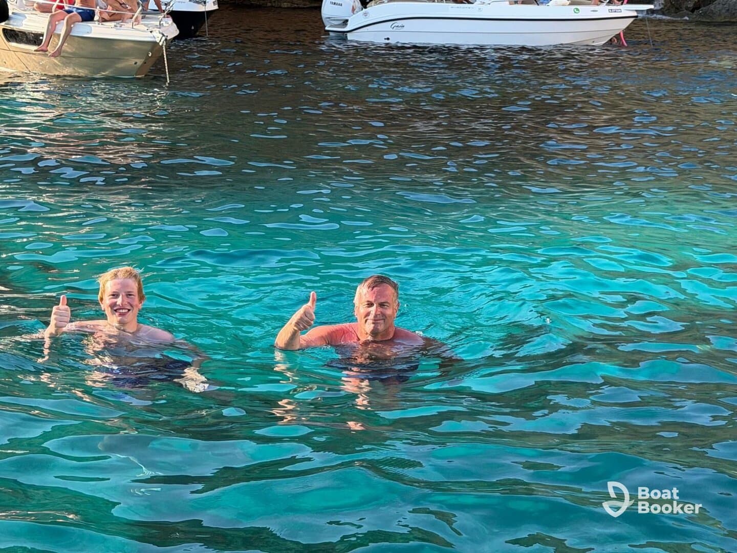 Two individuals enjoy a refreshing swim in crystal-clear waters, giving thumbs up for a perfect day on the water.