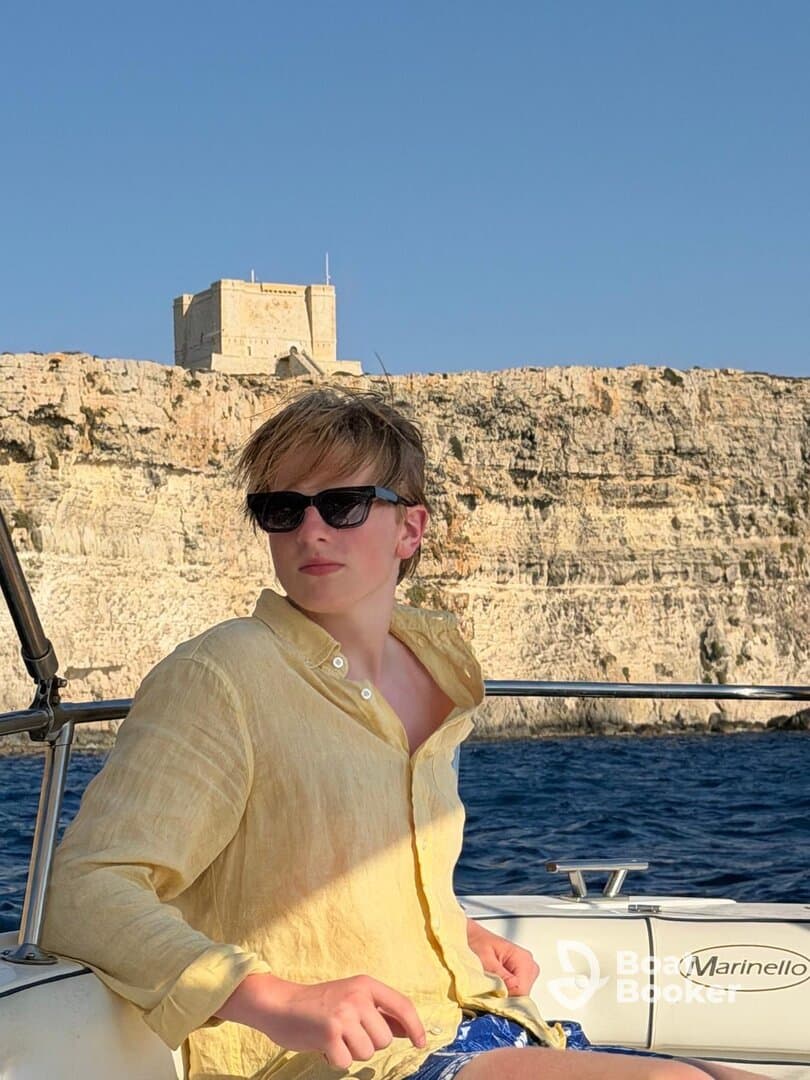 A young man enjoys a scenic boat ride with a historic landmark in the background, capturing the essence of summer adventures on the water.