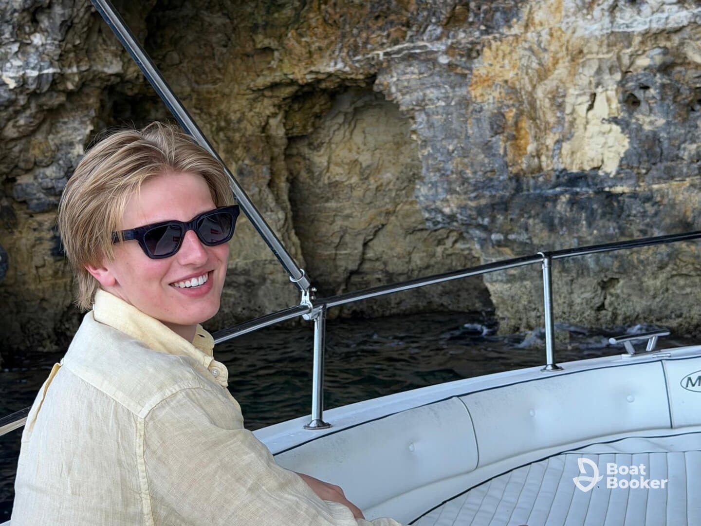 A young man enjoys a sunny day on a boat, smiling against a backdrop of rocky cliffs — perfect for capturing memorable moments on the water.