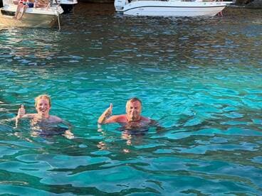 Two individuals enjoy a refreshing swim in crystal-clear waters, giving thumbs up for a perfect day on the water.
