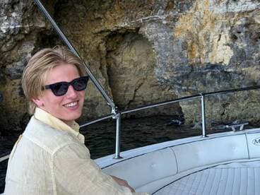 A young man enjoys a sunny day on a boat, smiling against a backdrop of rocky cliffs — perfect for capturing memorable moments on the water.