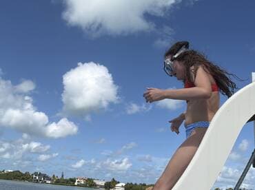 A young girl prepares to jump into the water while wearing snorkeling gear, capturing the excitement of a fun day on the water.