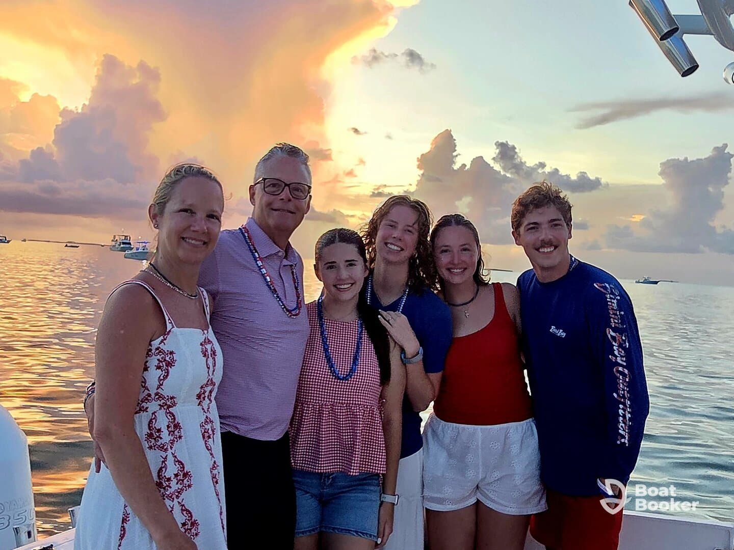 A joyful group of friends and family poses for a photo against a stunning sunset backdrop, capturing a memorable moment on the water.