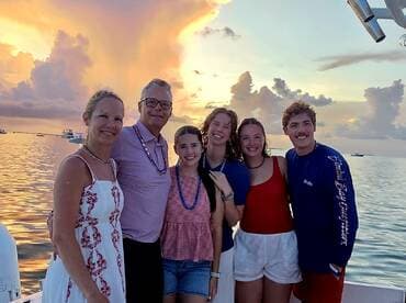 A joyful group of friends and family poses for a photo against a stunning sunset backdrop, capturing a memorable moment on the water.