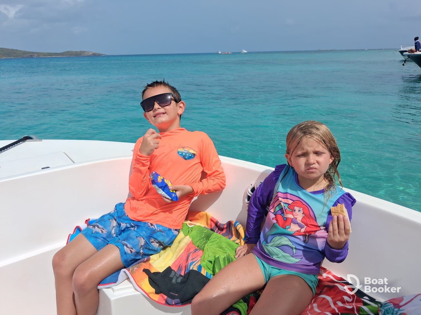 Two children enjoy snacks on a boat surrounded by beautiful turquoise waters, capturing a fun moment during their day on the water.