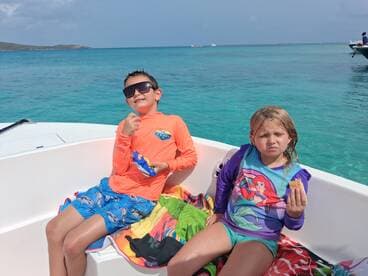 Two children enjoy snacks on a boat surrounded by beautiful turquoise waters, capturing a fun moment during their day on the water.