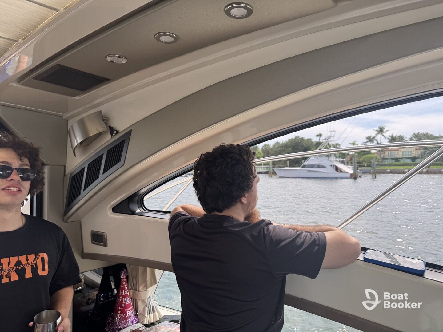 Two guests relax inside the cabin of a boat, enjoying the view through the window. The interior features comfortable seating, making it a perfect spot for leisure on the water.