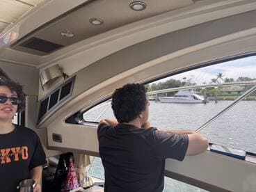 Two guests relax inside the cabin of a boat, enjoying the view through the window. The interior features comfortable seating, making it a perfect spot for leisure on the water.