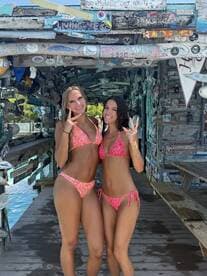 Two friends pose playfully in colorful bikinis at a lively waterfront location, capturing the essence of summer fun and celebration.