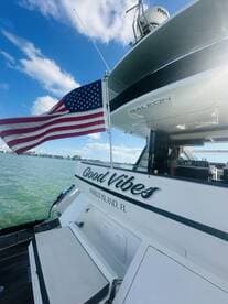 A stunning view of the 'Good Vibes' yacht featuring an American flag, showcasing the sleek design and inviting atmosphere of boating in Marco Island, FL.