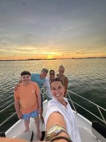A joyful group captures a sunset selfie aboard a boat, celebrating together against a stunning backdrop of the setting sun — perfect for family outings and memorable moments on the water.