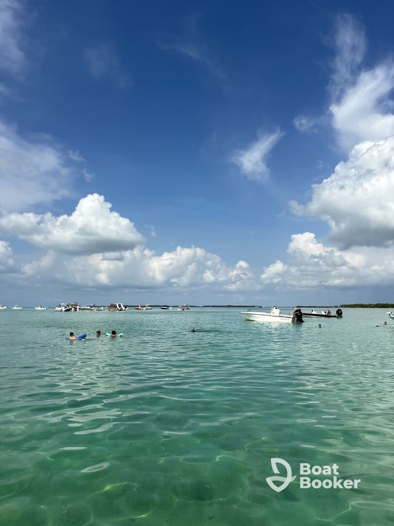 A lively scene of people swimming in clear turquoise waters, with boats anchored nearby — perfect for a fun day at the beach.