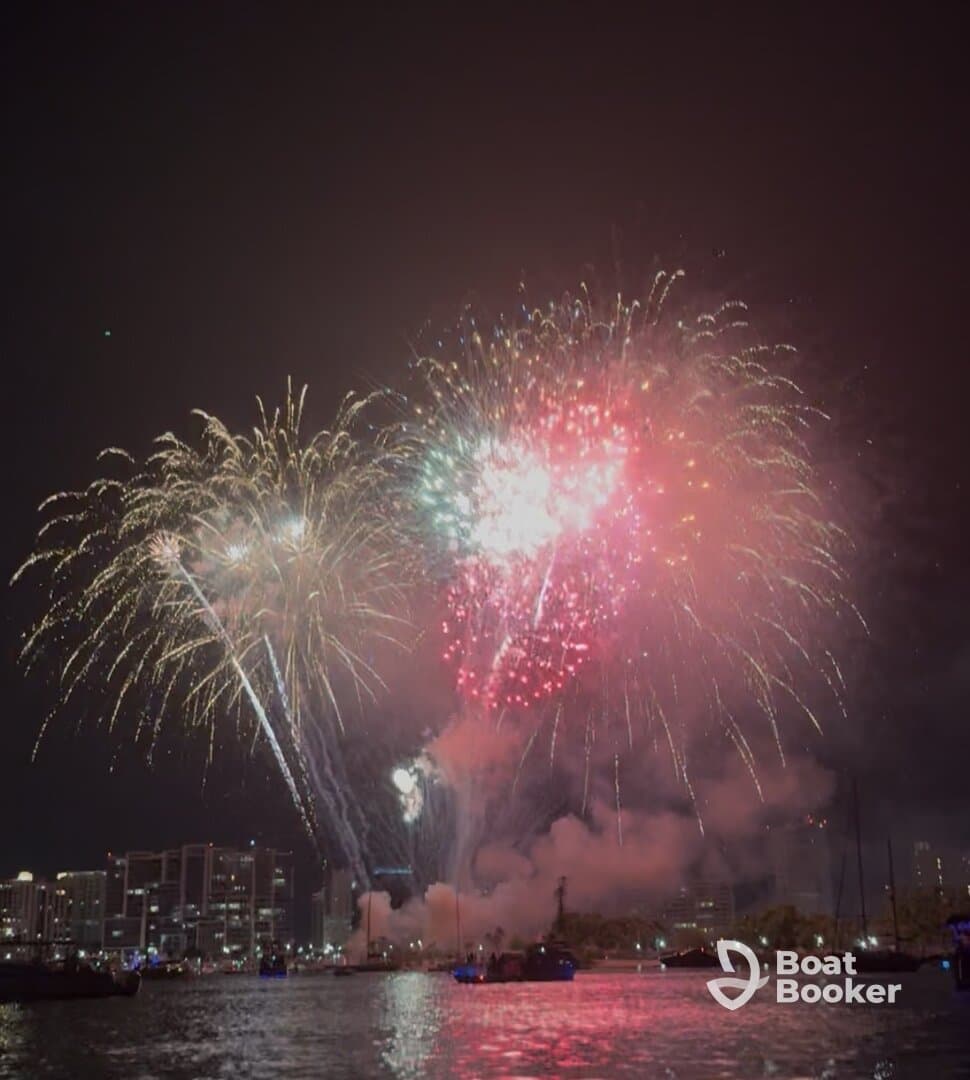 A stunning display of fireworks lights up the night sky over the city, creating a vibrant backdrop for celebrations on the water.