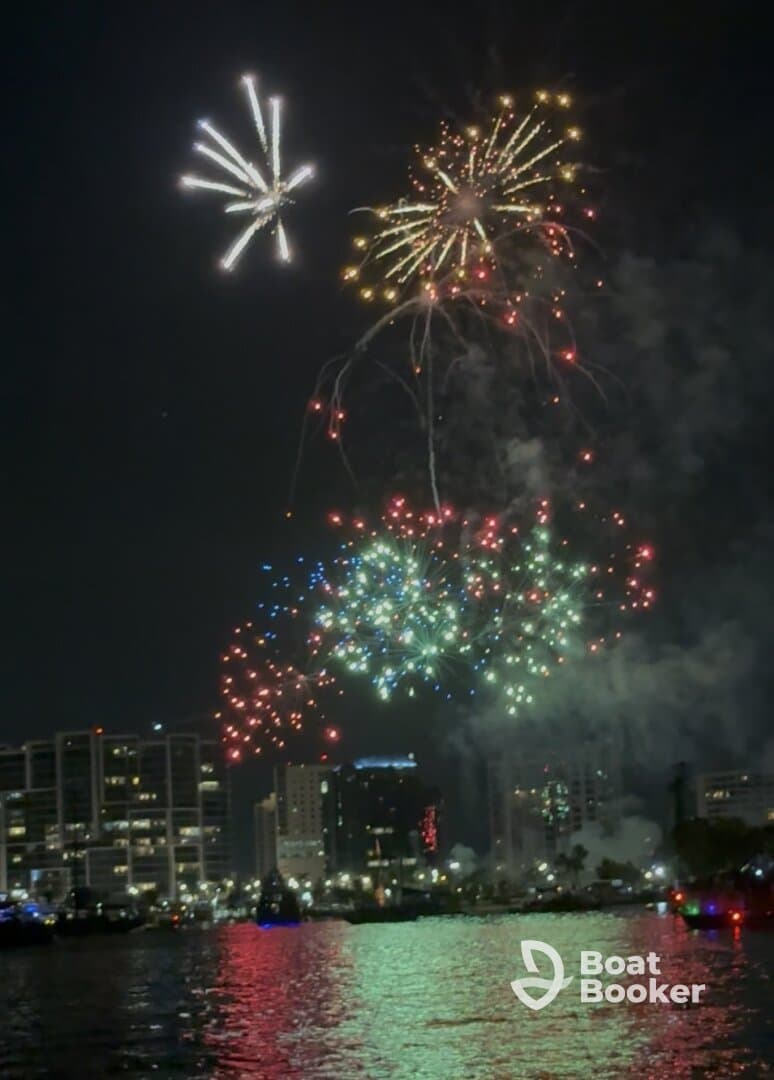 A stunning display of fireworks lights up the night sky over the city, creating a vibrant backdrop for a memorable boating experience.