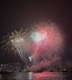 A stunning display of fireworks lights up the night sky over the city, creating a vibrant backdrop for celebrations on the water.
