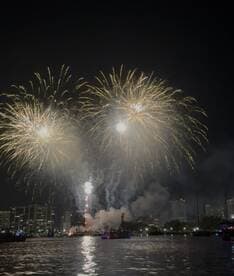 A stunning display of fireworks lights up the night sky over the city, creating a festive atmosphere perfect for celebrations on the water.