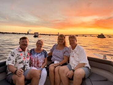 A cheerful group enjoys a sunset cruise on a boat, celebrating with drinks and laughter as the sun sets over the water.