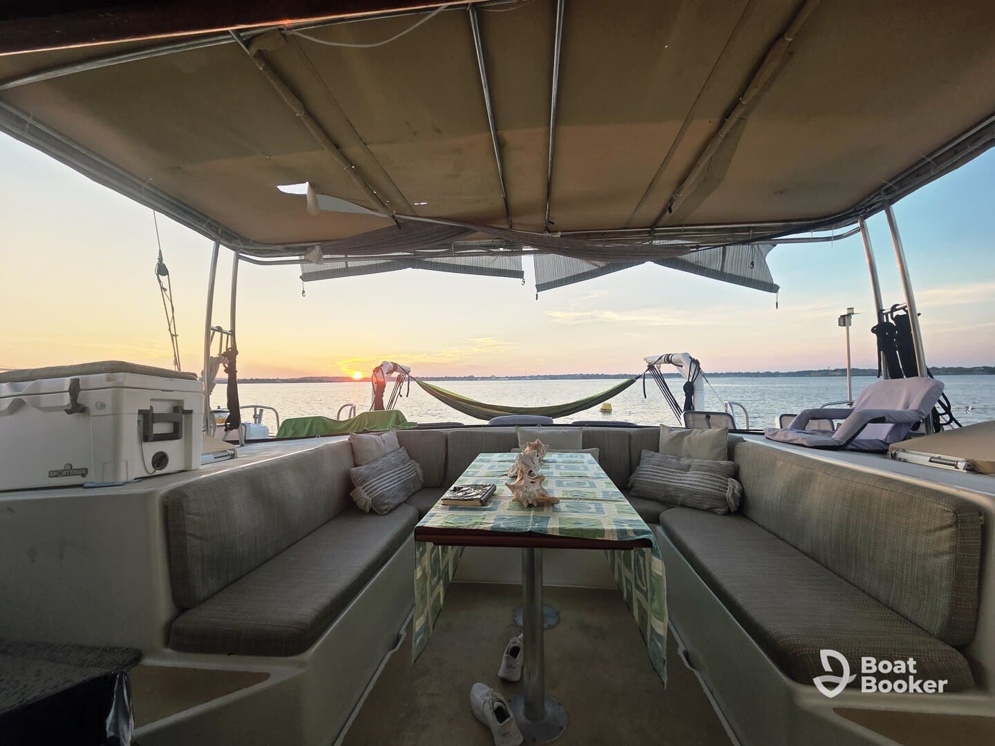 A cozy interior view of a boat's seating area, featuring a table set for relaxation with a beautiful sunset visible through the windows — perfect for enjoying serene moments on the water.