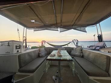A cozy interior view of a boat's seating area, featuring a table set for relaxation with a beautiful sunset visible through the windows — perfect for enjoying serene moments on the water.