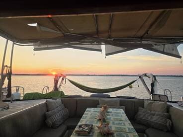 A serene view from the interior of a boat, showcasing a cozy seating area with a table and a beautiful sunset over the water — perfect for relaxing evenings on the water.
