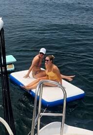 Two friends enjoy a sunny day on a floating mat in the water, capturing the essence of summer fun and relaxation on the water.