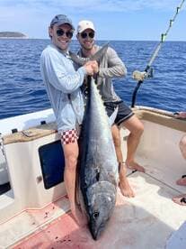Two friends proudly display their impressive catch of a tuna while fishing on a boat — a thrilling moment for any angler.