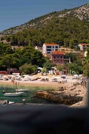 A picturesque beach scene with sunbathers and swimmers enjoying the clear waters, set against a backdrop of charming coastal homes and lush greenery.