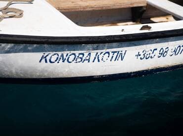 Close-up of a boat's name and contact number, showcasing the vessel's details against a serene turquoise backdrop.