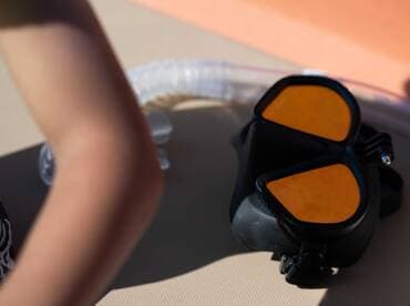 A close-up of snorkel gear laid out on a boat, with a child's arm visible, ready for underwater adventures.