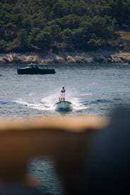 A person enjoys a thrilling ride on a small boat, creating a splash in the serene waters surrounded by lush greenery — a perfect snapshot of summer adventures on the water.
