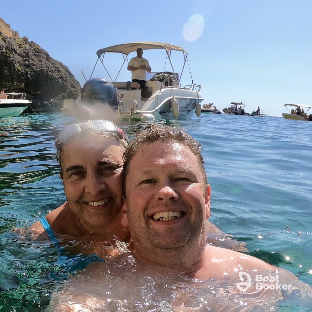A joyful couple enjoys a refreshing swim in crystal-clear waters, with a boat in the background, capturing the essence of a perfect day on the water.