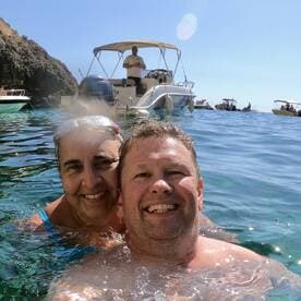 A joyful couple enjoys a refreshing swim in crystal-clear waters, with a boat in the background, capturing the essence of a perfect day on the water.