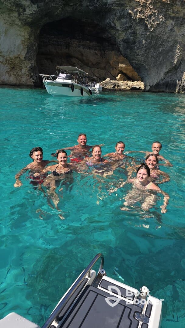 A joyful group of friends enjoys a refreshing swim in crystal-clear turquoise waters, with a boat anchored nearby, perfect for a fun day out on the water.