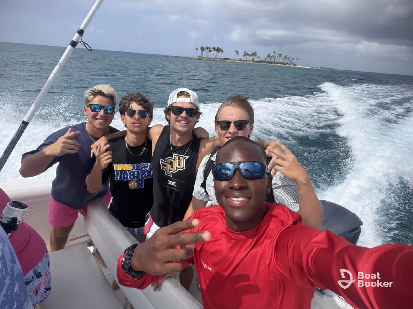 A group of friends poses for a fun selfie on a boat, enjoying their time on the water with a beautiful island in the background.