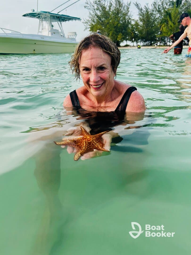 A woman joyfully holds a starfish while swimming in clear waters, showcasing a memorable wildlife interaction in a tropical paradise.