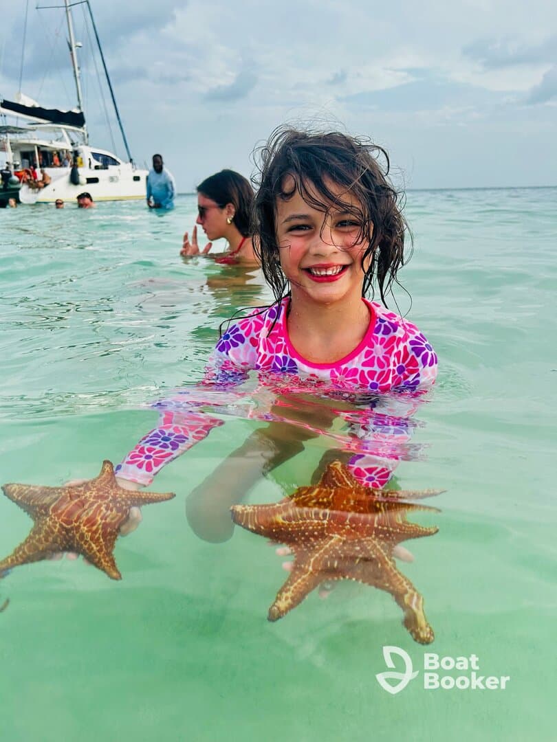A joyful child holds starfish while swimming in clear waters, showcasing a delightful interaction with marine wildlife — a memorable experience for young adventurers.
