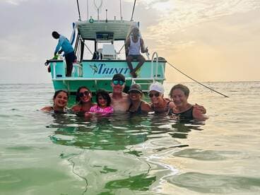 A joyful group of family members enjoys a refreshing swim in the ocean, with their boat anchored nearby, creating unforgettable memories during a sunset cruise.