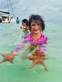 A joyful child holds starfish while swimming in clear waters, showcasing a delightful interaction with marine wildlife — a memorable experience for young adventurers.
