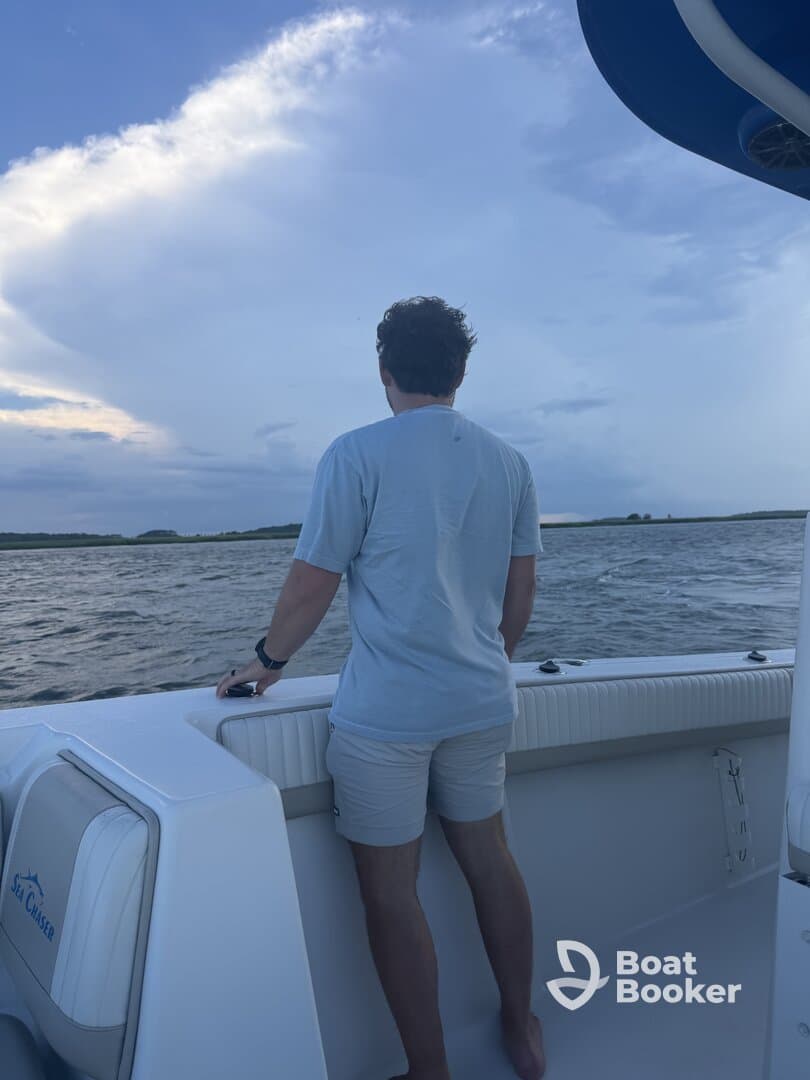 A man stands on the deck of a boat, gazing out at the ocean under a dramatic sky — a serene moment capturing the beauty of the water and clouds.