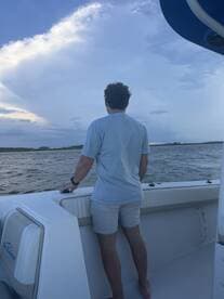 A man stands on the deck of a boat, gazing out at the ocean under a dramatic sky — a serene moment capturing the beauty of the water and clouds.