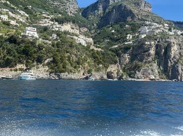 A stunning view of a yacht cruising along the Amalfi Coast, surrounded by picturesque cliffs and lush greenery, perfect for exploring the beautiful Italian coastline.
