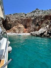 A picturesque view of a secluded beach with people enjoying the sun and water, framed by stunning rocky cliffs — an ideal spot for a relaxing day on the water.