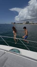 A couple joyfully jumps off the side of a boat into the water, capturing the thrill of summer fun on the water.
