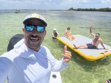 A joyful group enjoys a sunny day on the water, featuring a floating mat and a friendly dog — perfect for summer fun and family outings.